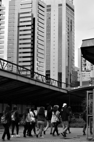 Prédios e pessoas caminhando numa calçada, em preto e branco